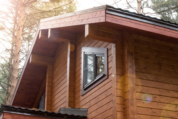 Detail dřevostavby s oknem na pozadí lesa