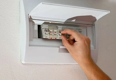 Ruka přepíná jistič v rozvaděči pro elektroinstalaci.
