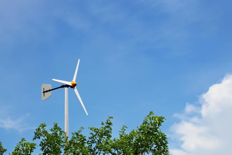 Malá větrná elektrárna na sloupě mezi stromy pod modrou oblohou.