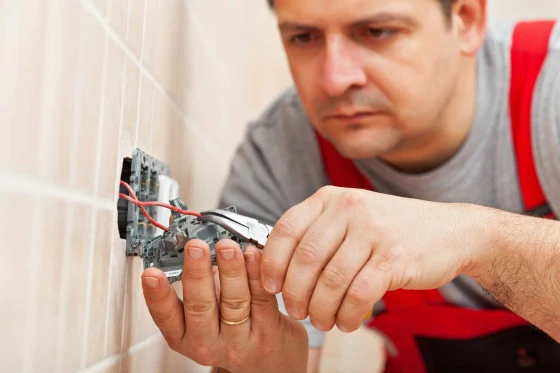 Elektrikář zapojuje dráty do elektrické zásuvky na zdi.