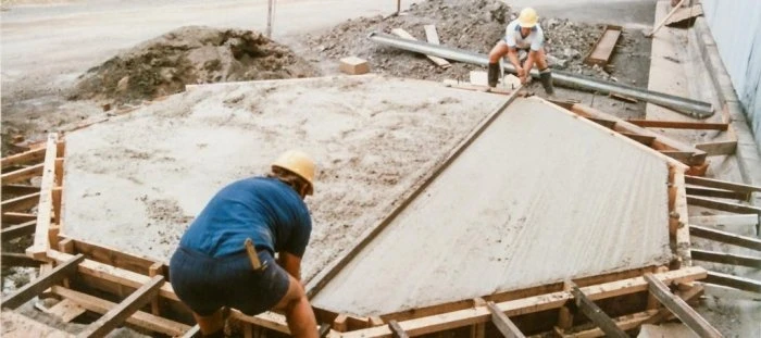 Dva dělníci nalévají beton do základové desky budovy.