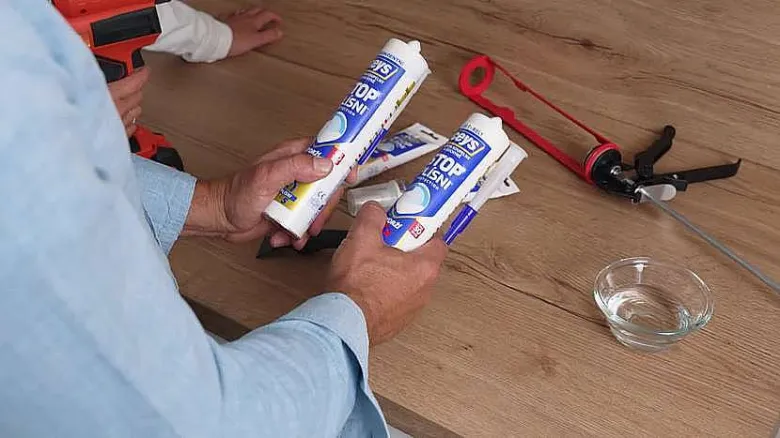 Muži drží dvě tuby silikonu vedle pistole na aplikaci kolem vany.