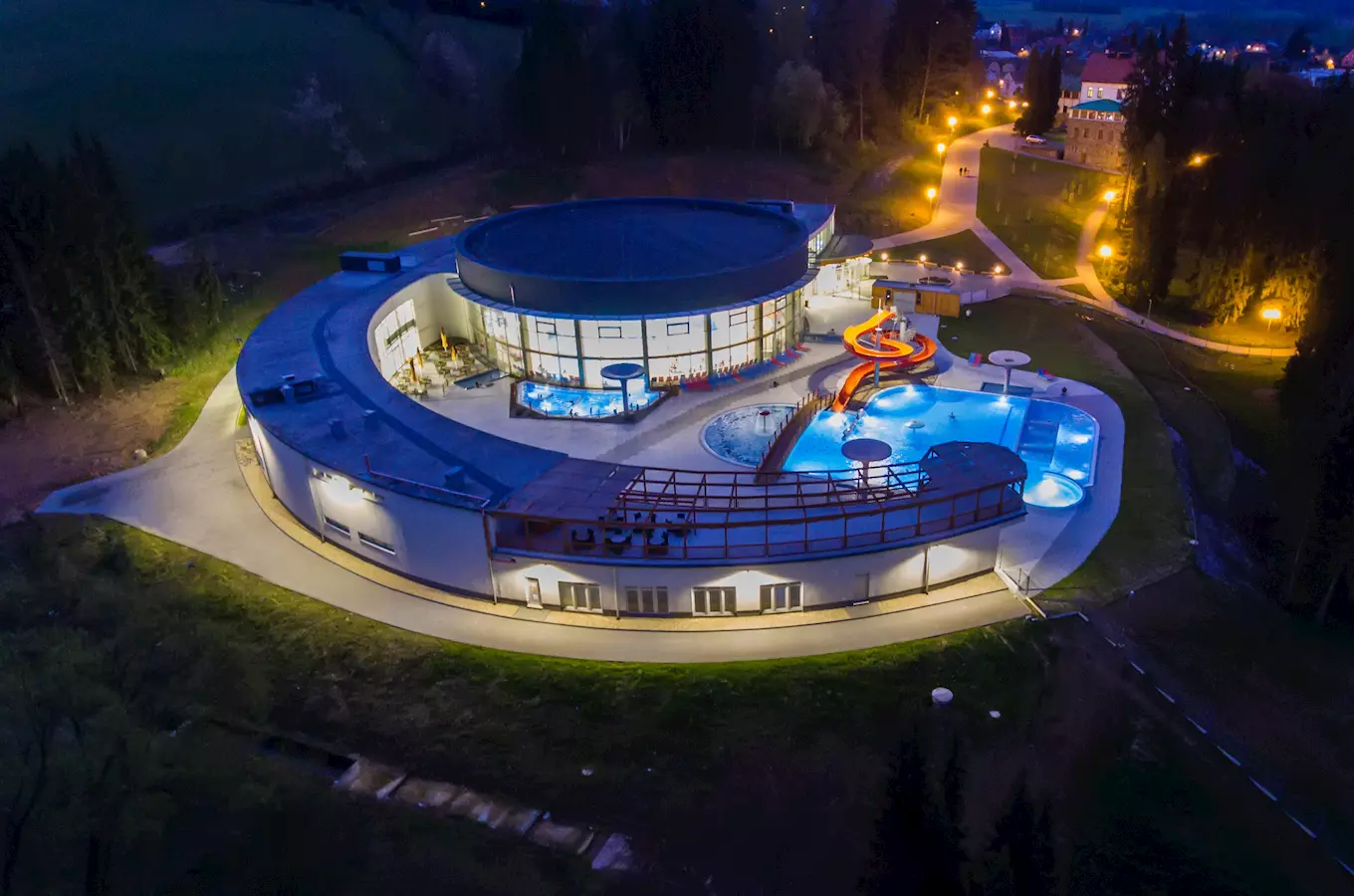 Noční pohled na venkovní bazén s vodním hřištěm pro děti.