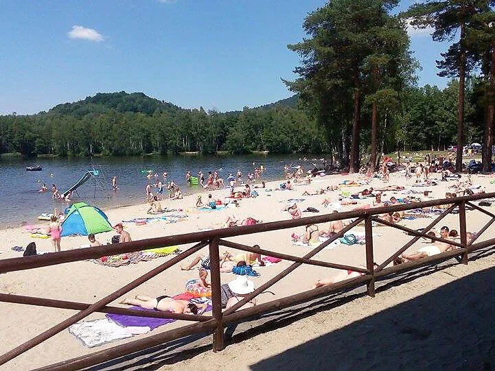 Lidé na pláži u jezera v Sloupu s hory v pozadí.
