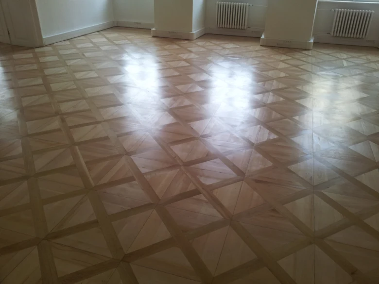 Opravená parketová podlaha s geometrickým vzorem po renovaci.