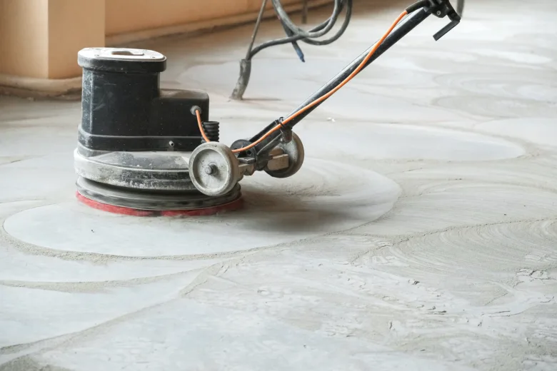 Černý stroj na leštění podlahy pracuje na betonové ploše.