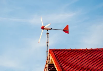 Malá domácí větrná turbína na střeše domu pod modrou oblohou.