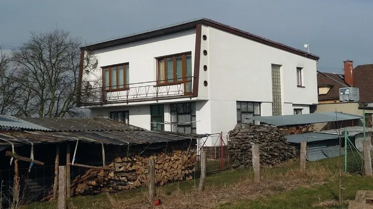Moderní bílý dům s dřevěným ohništěm na pozadí venkovského prostředí.