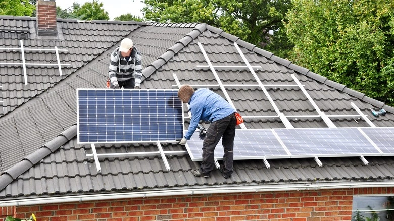 Dva pracovníci montují fotovoltaické panely na střechu.