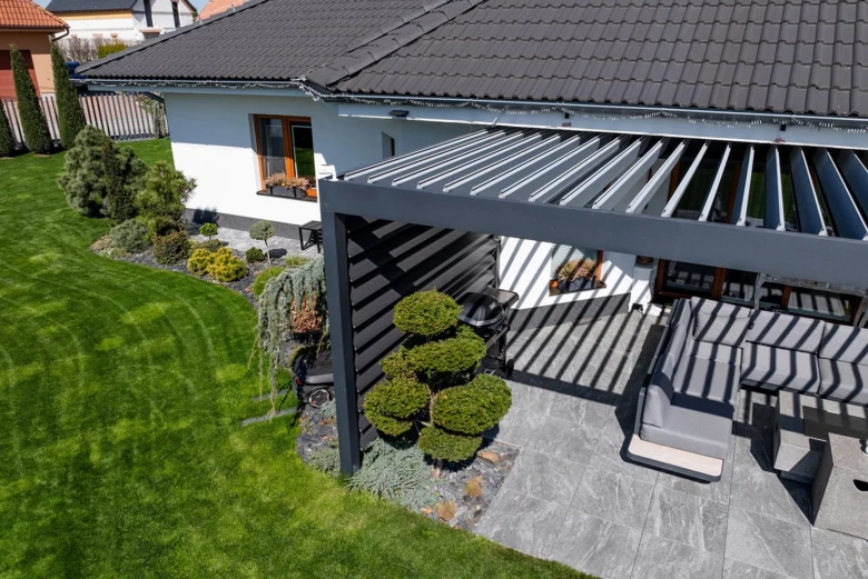 Moderní šedá kovová pergola přistavěná k domu s kamennou terasou.