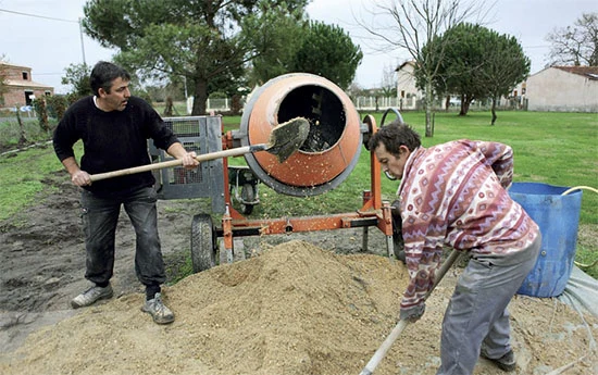 Muži míchají zdivou maltu pomocí betonového smíchávače.