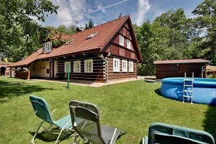 Dřevěný domek s bazénem a židlemi na trávníku.