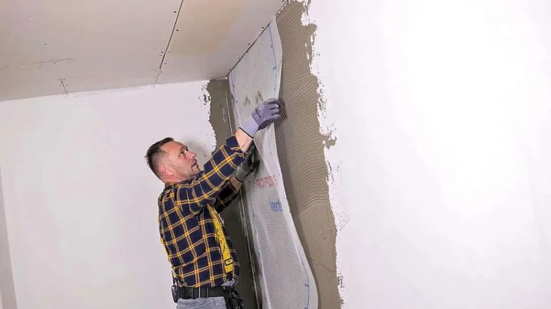 Muž lepi perlinkovou matku na stěnu v rohu.