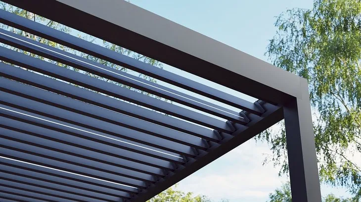 Bioklimatická pergola s nastavitelnou střechou na pozadí stromů.