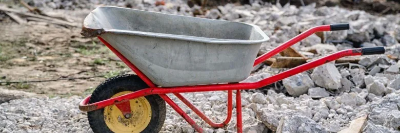 Červené stavební kolečko na hromadě betonu a sutiny.