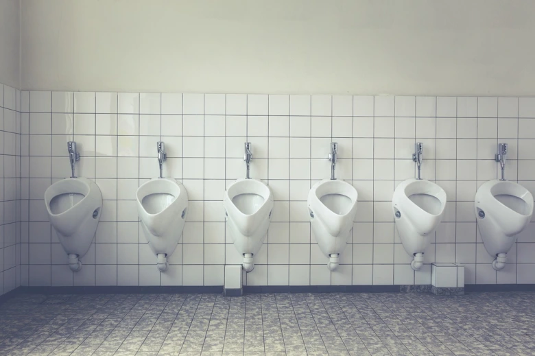 Řada bílých pisoárů namontovaných na dlaždicové stěně v koupelně.