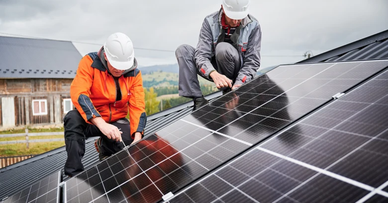 Dva dělníci montují fotovoltaické panely na střechu.