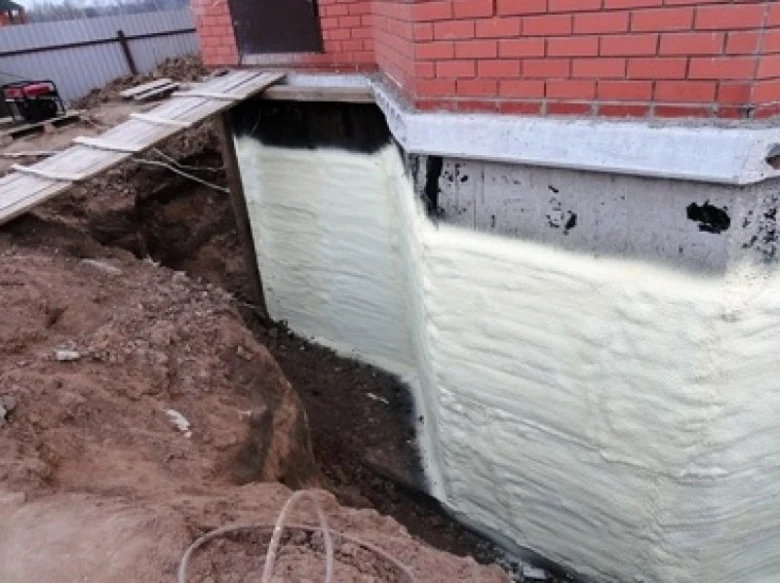 Bílá polyuretanová pěna se nanáší na betonovou základnu domu.