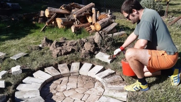 Muž staví kruhové ohniště z cihel na zahradě.