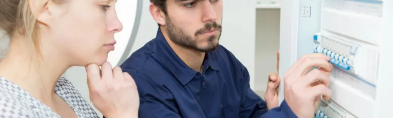 Elektroinženýr nastavuje jističe v rozvaděči před ženou.