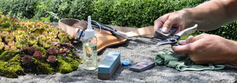 Člověk brousí zahradní nůžky na kamenné ploše venku.