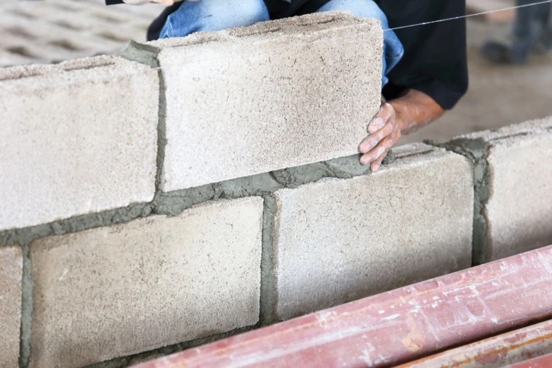 Stavebník kladí betonové cihly do zdiva při stavbě plotu.