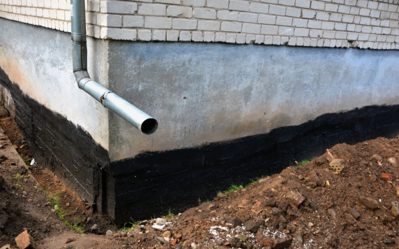 Černá hydroizolace na základě budovy vedle odvodňovacího potrubí.