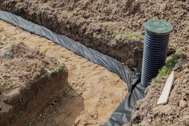Instalace drenážního systému s hadicí v příkopu na zahradě.