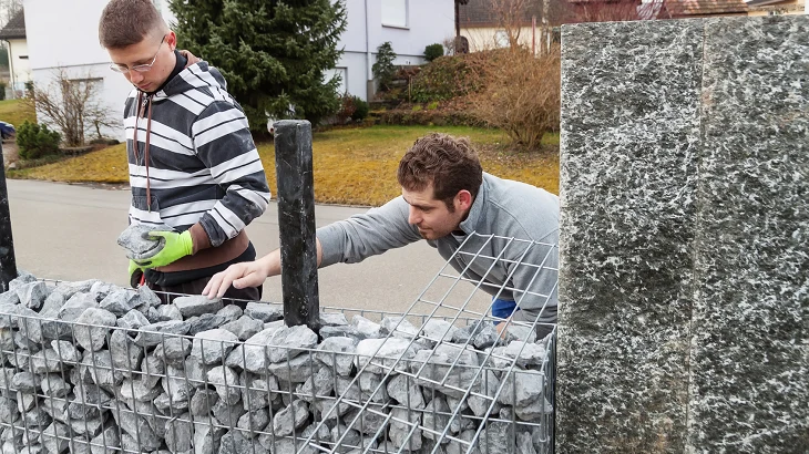 Muži plní drátěné koše kameny pro stavbu zahradního zdi.