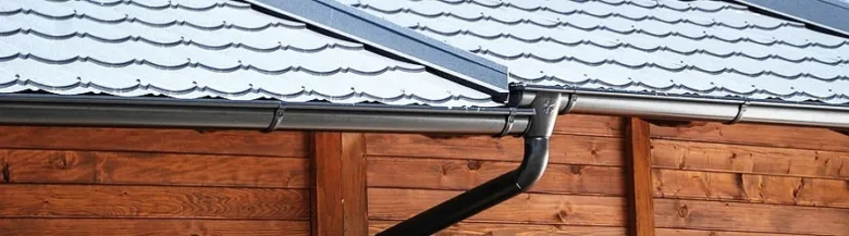 Černý plastový okap na střeše nad dřevěnou fasádou.