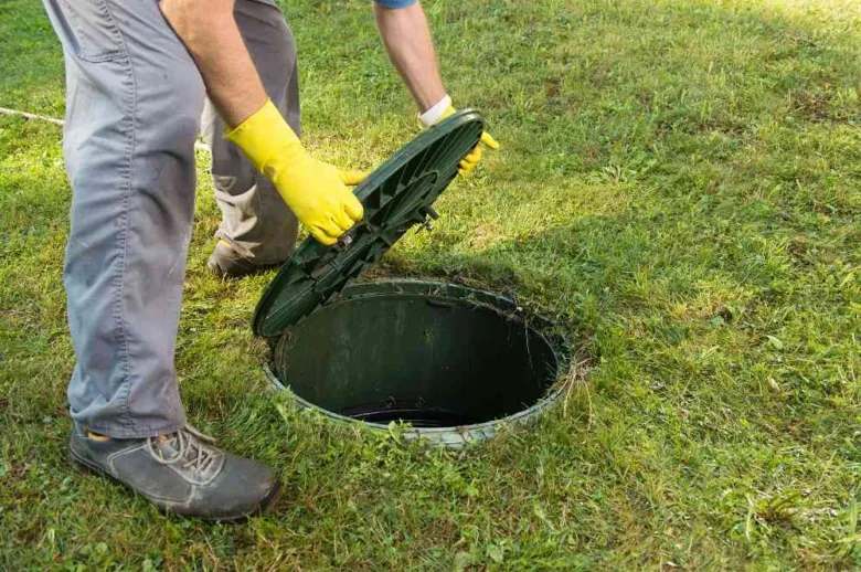 Muž otevírá poklop septiku na trávníku.