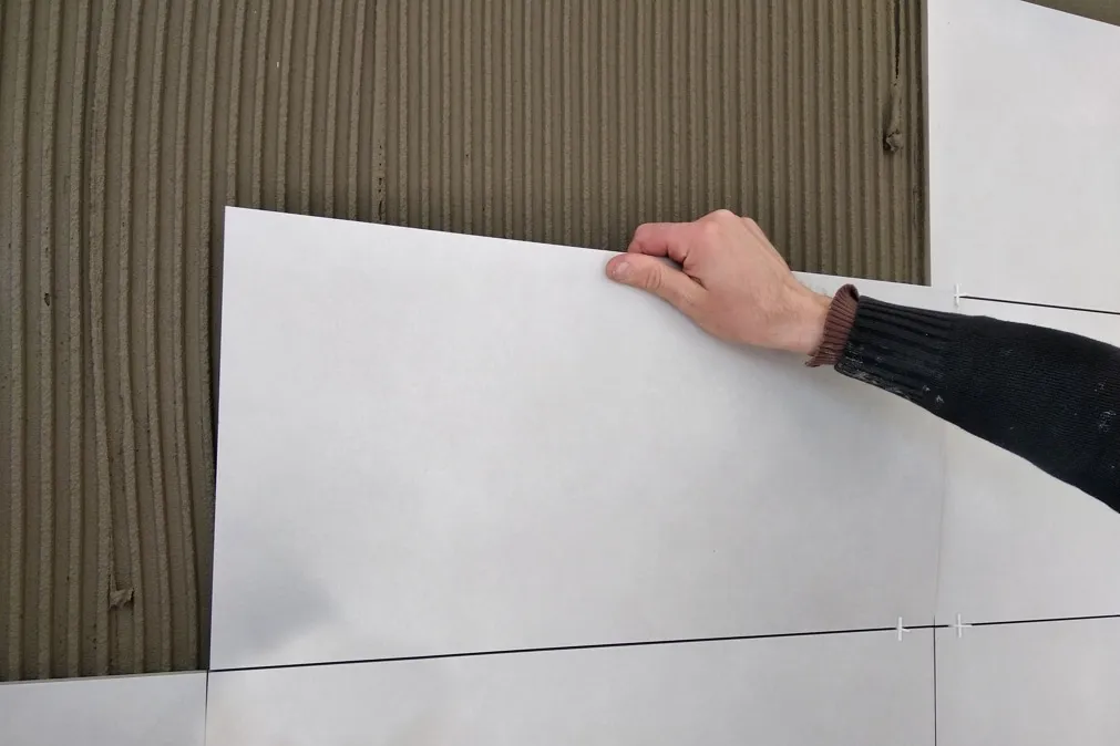 Ruční instalace velkoformátové dlažby na vnitřní stěnu.