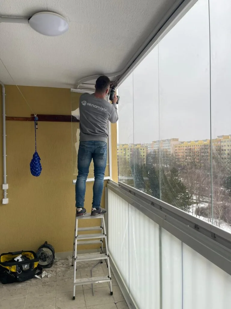 Montáž zasklení balkonu s pracovníkem na žebříku.