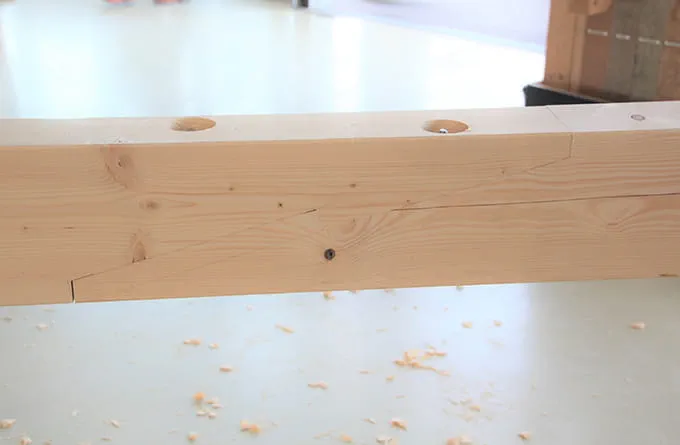 Dřevěný trám s předvrtanými otvory pro tesářské spoje na pracovním stole.