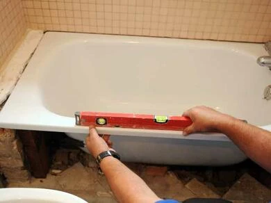 Člověk kontroluje úroveň okraje staré vany při výměně.