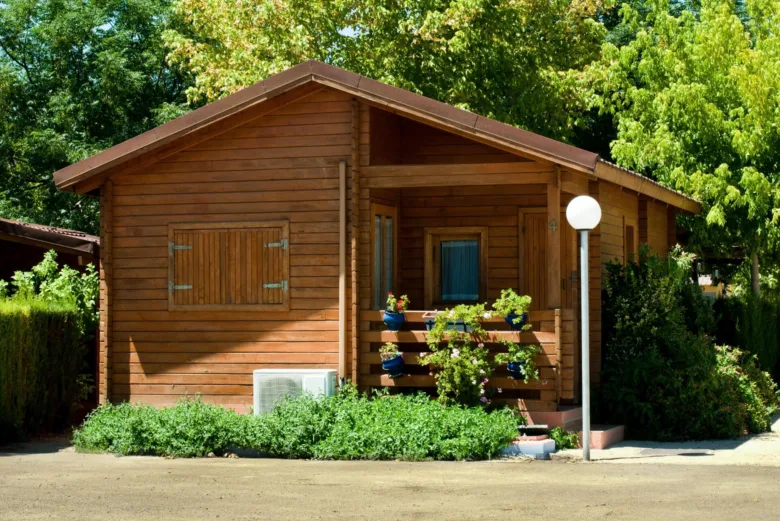 Dřevěný zahradní domek s okny a balkónem uprostřed zelené zahrady.