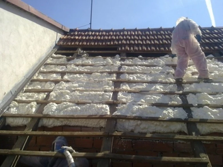 Pracovník aplikuje izolační pěnu mezi střešní trámy.