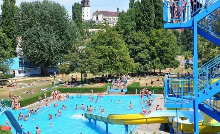 Venkovní bazén v Praze s tobogány a lidmi koupející se.