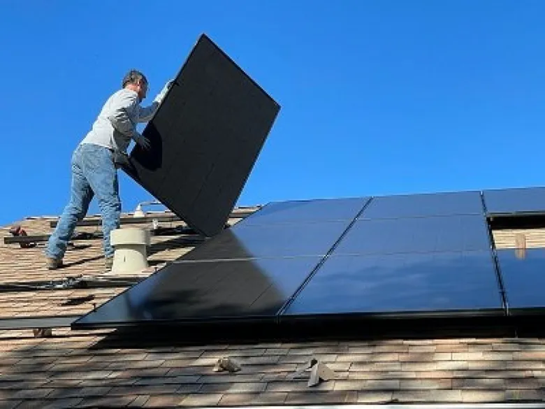 Muž montuje fotovoltaický panel na střechu domu.