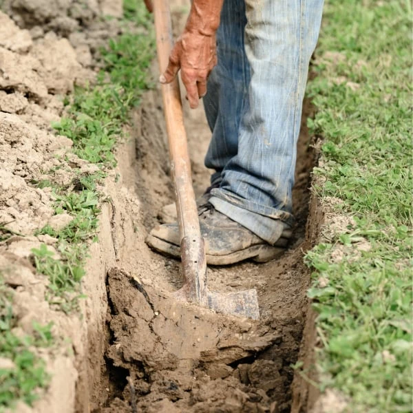 Člověk kopá drenážní příkop lopatou v zemi.