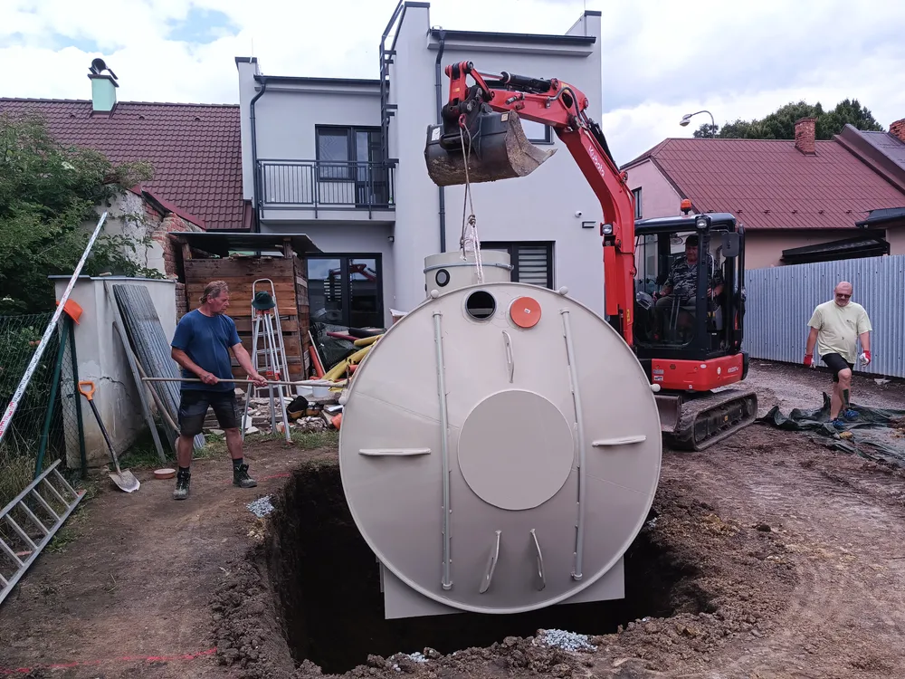 Instalace septiku do jámy pomocí výkopového stroje na pozemku.