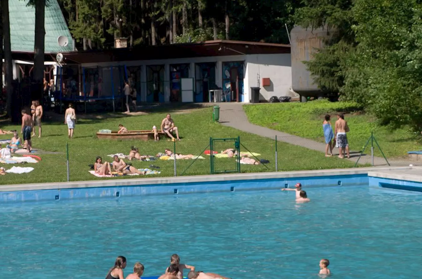 Venkovní bazén s lidmi plavajícími na trávníku v parku.