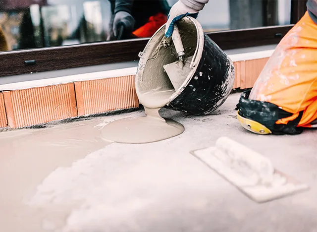 Pracovník nalévá voděodolný maltový roztok na betonovou plochu pro hydroizolaci.