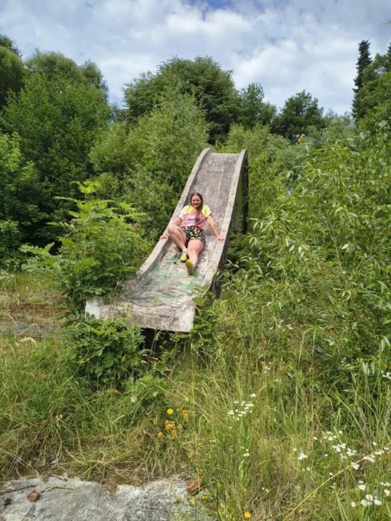 Žena sedí na opuštěném betonu skluzavce v zarostlé přírodě.