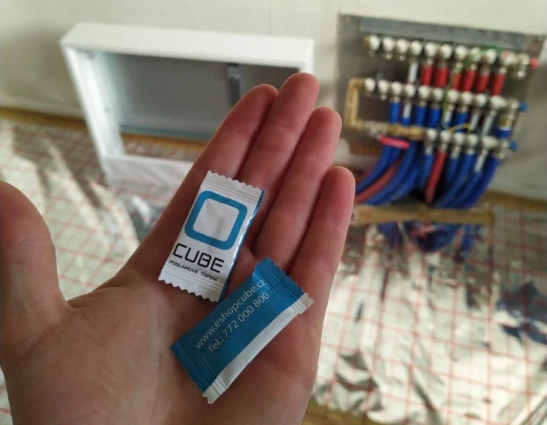 Ruce drží balíčky CUBE vedle rozvodného tělesa pro podlahové topení.
