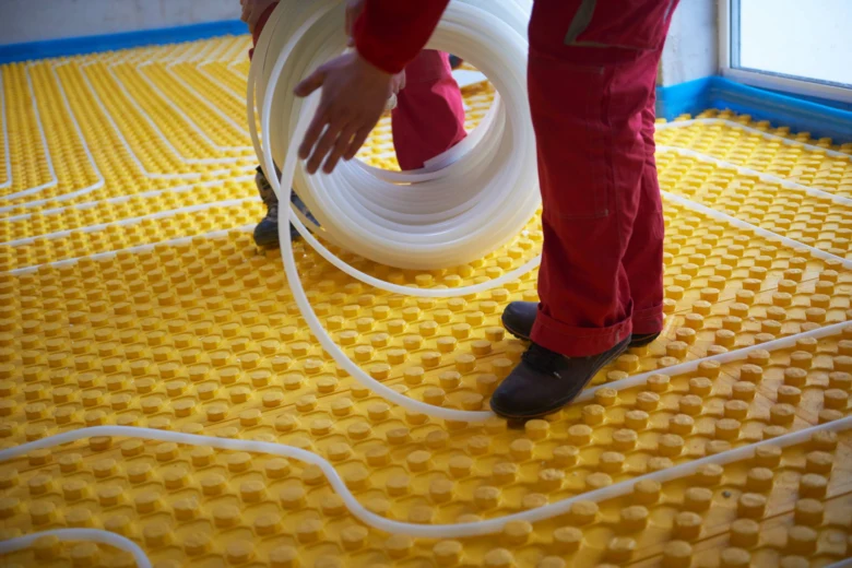 Instalace podlahového topení s rozvodem potrubí na žluté desce.