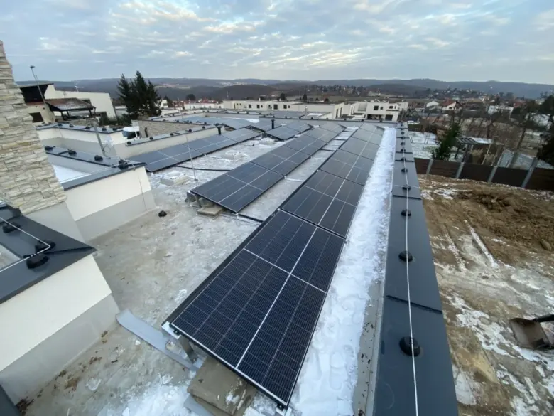 Fotovoltaické panely na střeše v zimě s výhledem do města.