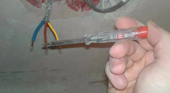 Ruka drží testovací šroubovák u odhalených vodičů pro zapojení světla.