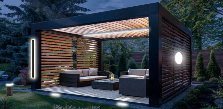 Moderní osvětlená pergola s venkovním nábytkem v zahradě večer.