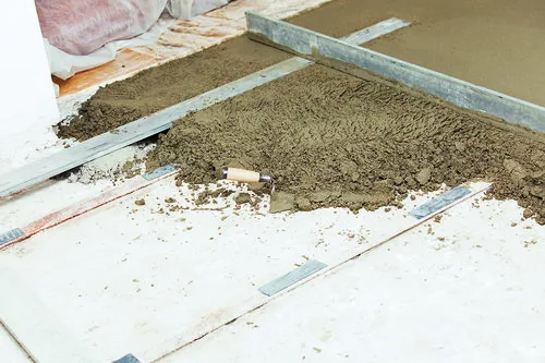 Mokrý beton se nalévá mezi lišty pro vyrovnání podlahy.